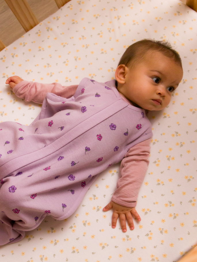 Baby in a purple merino sleeping bag lying in a cot 
