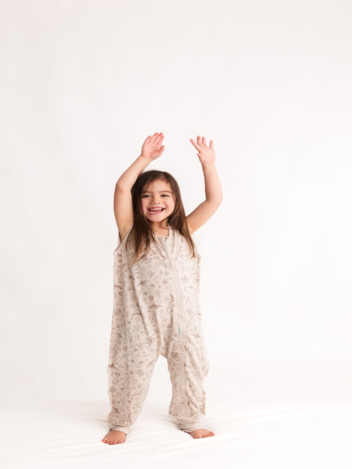 Child wearing a sand coloured woolbabe sleeping suit with hands up in a studio setting