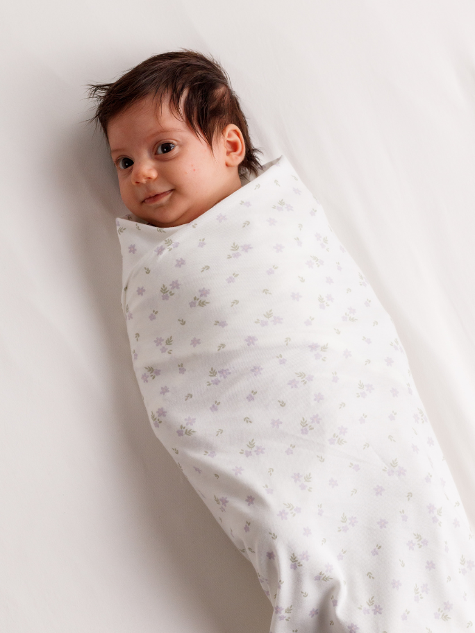 Baby in lilac daisy cotton swaddle on a light background