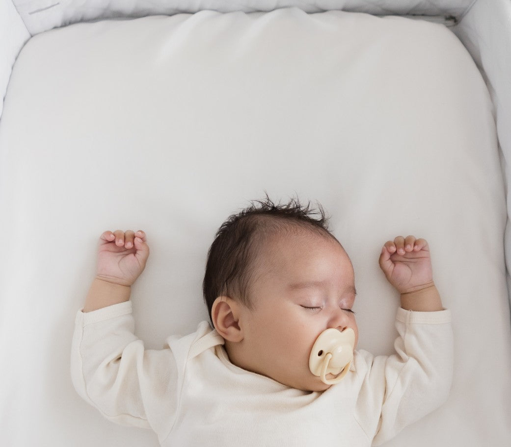 Baby Sleeping with arms up and dummy in mouth in a co-sleeper