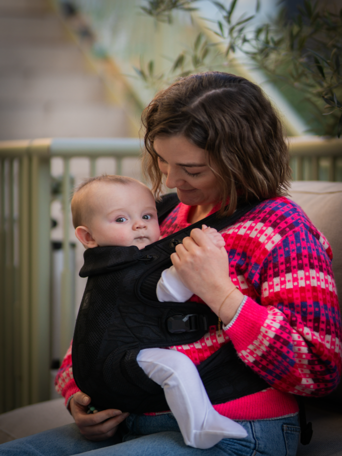 A mother wearing her baby in a Carifit baby carrier in an outdoor setting