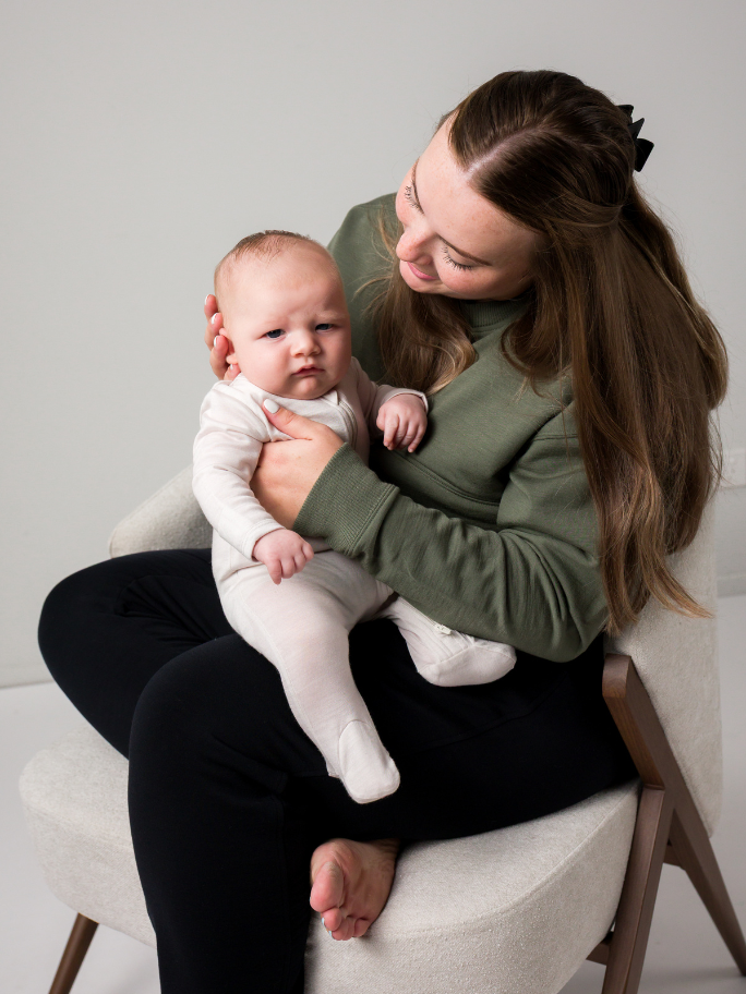 Mum holding her baby in a studio setting, wearing an olive fleece jumper