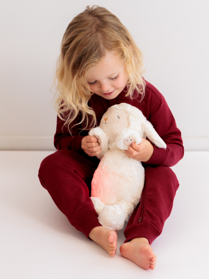 Child wearing fleece red tracksuit and playing with cream lou lou lamb with red light on belly