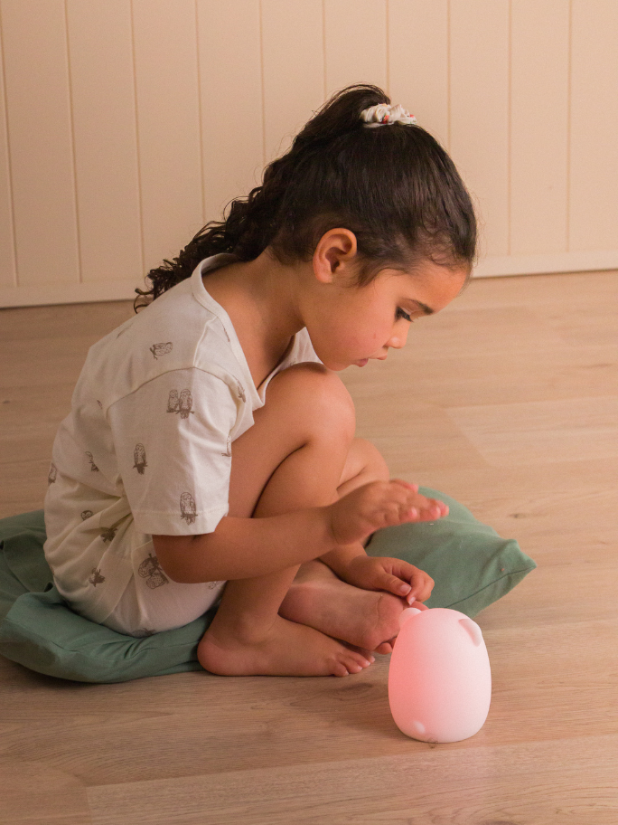 Toddler wearing soft cream pyjamas playing with a light to rise sound machine