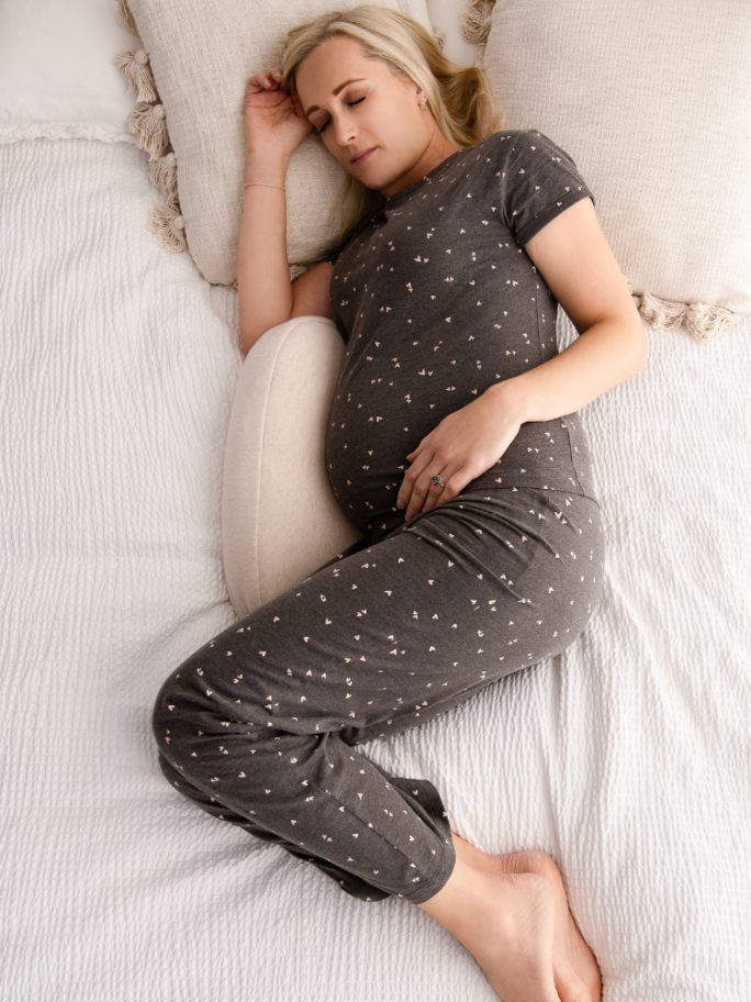 Pregnant woman in pyjama's sleeping on a bed with pregnancy pillow