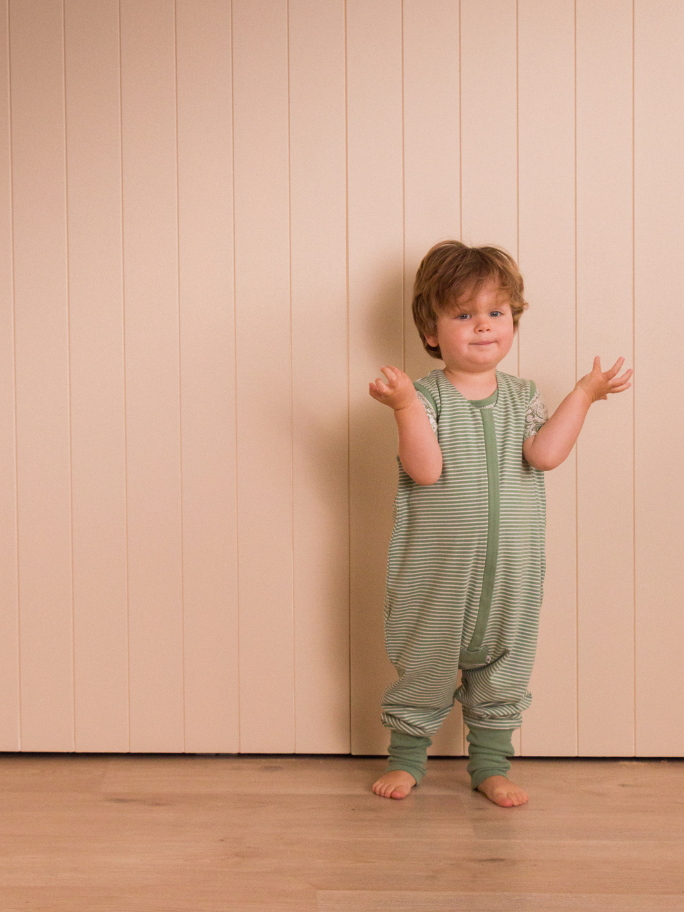 Toddler wearing a green and white striped sleeping suit in a studio setting