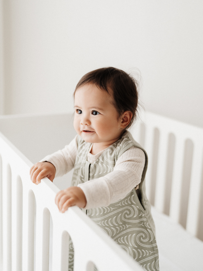 Baby standing up in white cot with smile