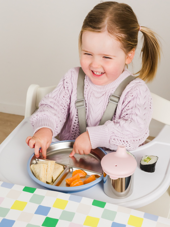 Toddler in highchair with nestling stainless steel flatware eating lunch