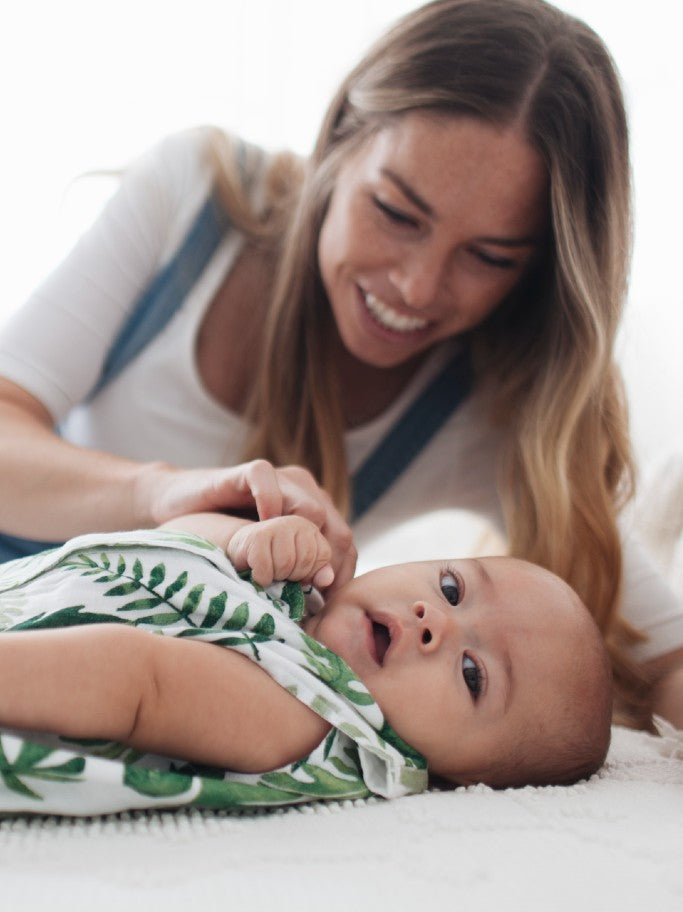 A baby wearing a tropical leaf sleeping bag while a mother smiles above