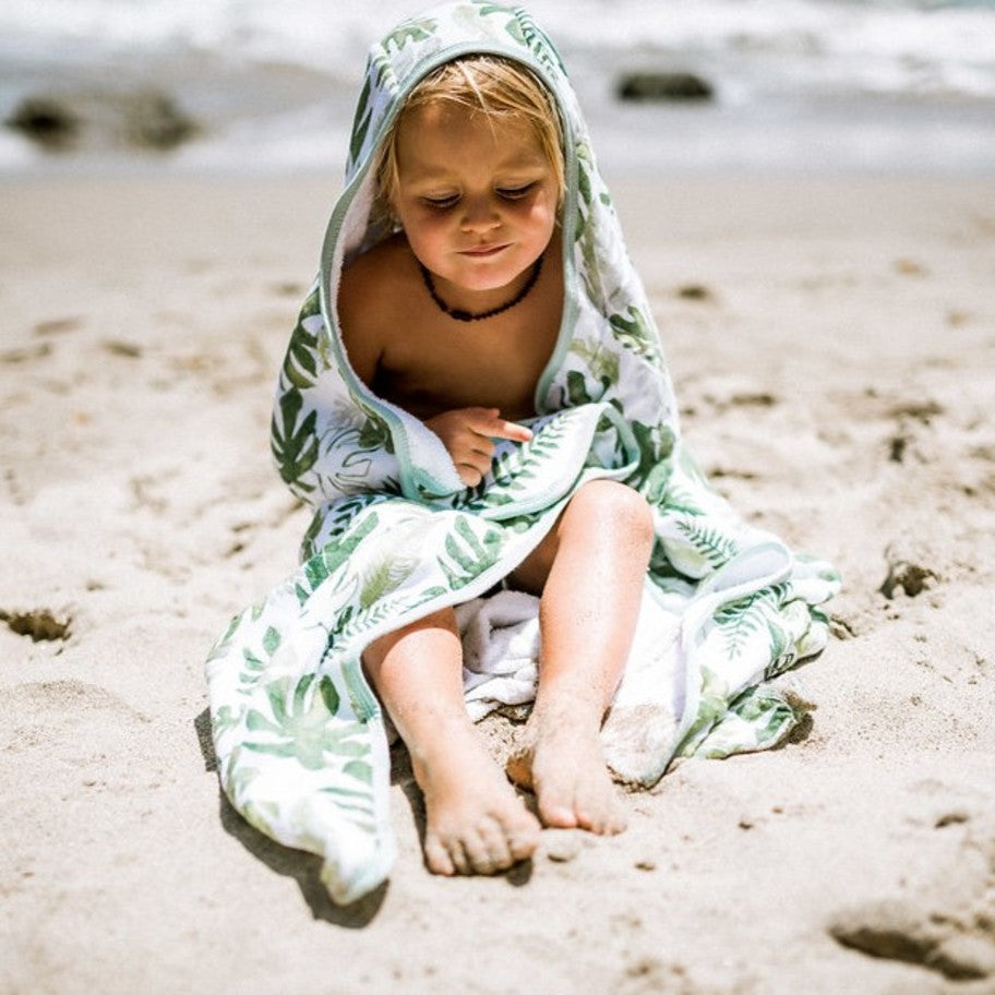 Toddler wearing a tropical leaf towel on the beach