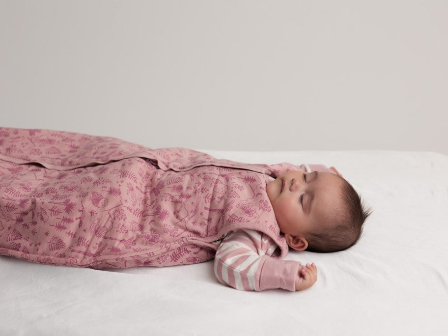 Baby sleeping on a white bed wearing a pink duvet sleeping bag and striped PJ suit 