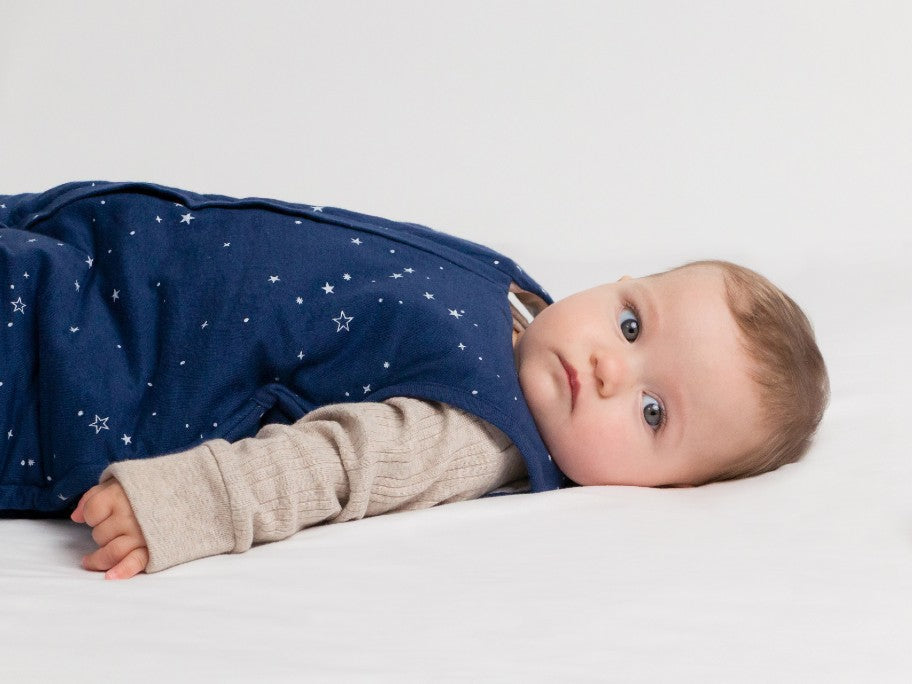 A baby wearing a dark blue sleeping bag with star pattern and beige ribbed long sleeve shirt