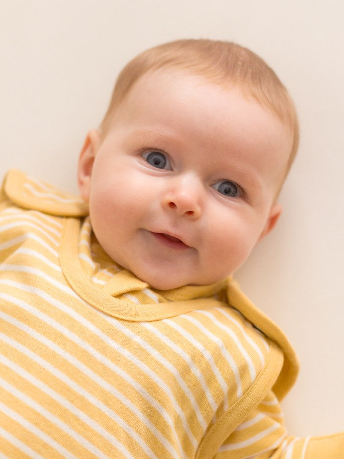 A small baby wearing a yellow striped sleeping bag with domes at the shoulder