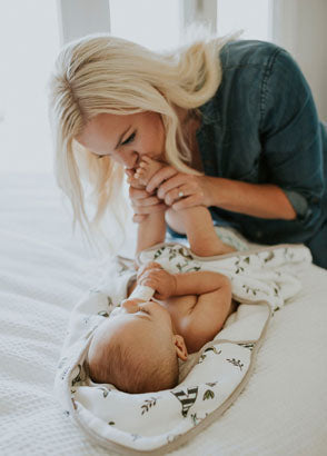 Baby wrapped in forrest friends towel enjoying kisses on his feet from mother