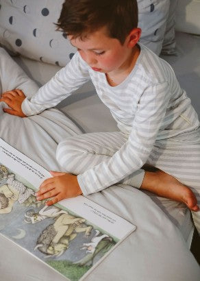 Boy reading a book on bed with the sleep store organic cotton bedding wearing Woolbabe pyjamas