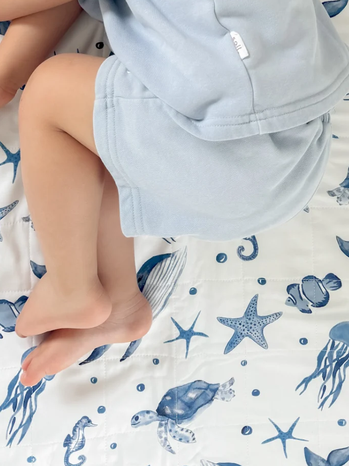Toddler laying on a brolly sheet with ocean theme blue print and white background