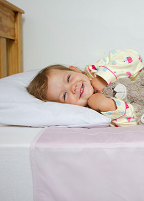 Child cuddling teddy resting in bed fitted with pink brolly sheet