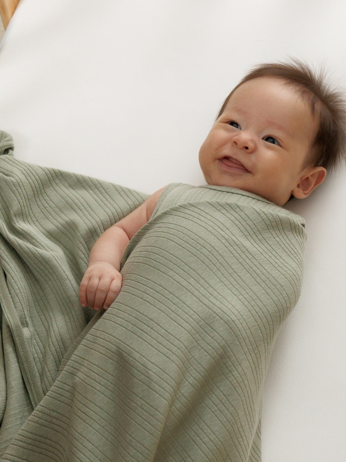 Smiling baby wrapped in green ribbed blanket and singletsuit