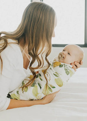 Baby swaddled in muslin with green pattern and dummy, being held by mum
