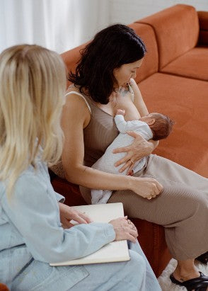 Two women sitting on a couch, one is breastfeeding