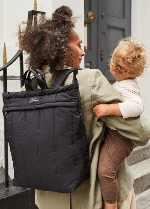Lady carrying Finnson rae nappy bag backpack on back and baby in arms on hip