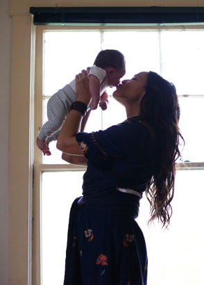 Mother kissing newborn while holding him up