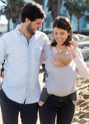Mum and dad walking together on beach with mum using Boba bliss hybrid baby carrier in grey