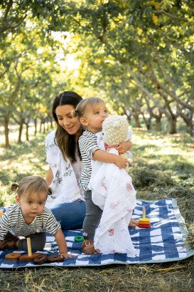 Mum with two toddlers sitting on a little unicorn outdoor picnic blanket navy plaid camping with a baby doll