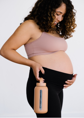 Pregnant mum looking at bump and carrying bink mama bottle in honey
