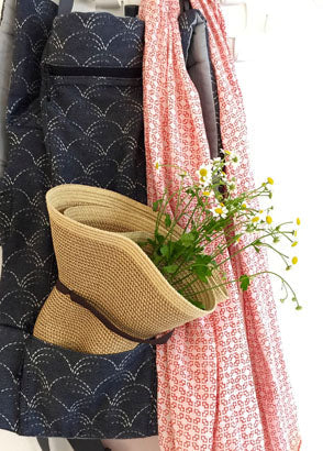 Straw hat with flowers inside carrier pocket hung on coat rack adorned with salmon muslin swaddle