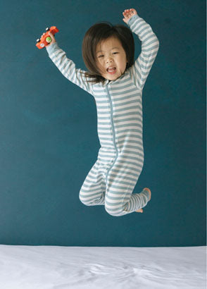 Toddler jumping on bed as she wears her Woolbabe tide sleeping suit