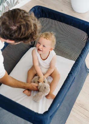Toddler sitting in the sleep store drift travel cot looking up at her dad