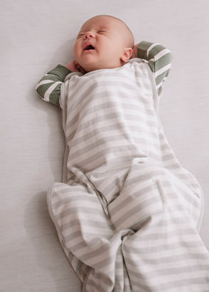 Newborn in a woolbabe sleeping bag stretching on a white surface
