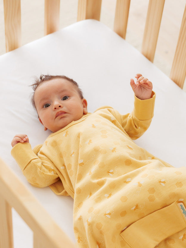baby lying in a cot wearing a yellow newborn sleeping bag