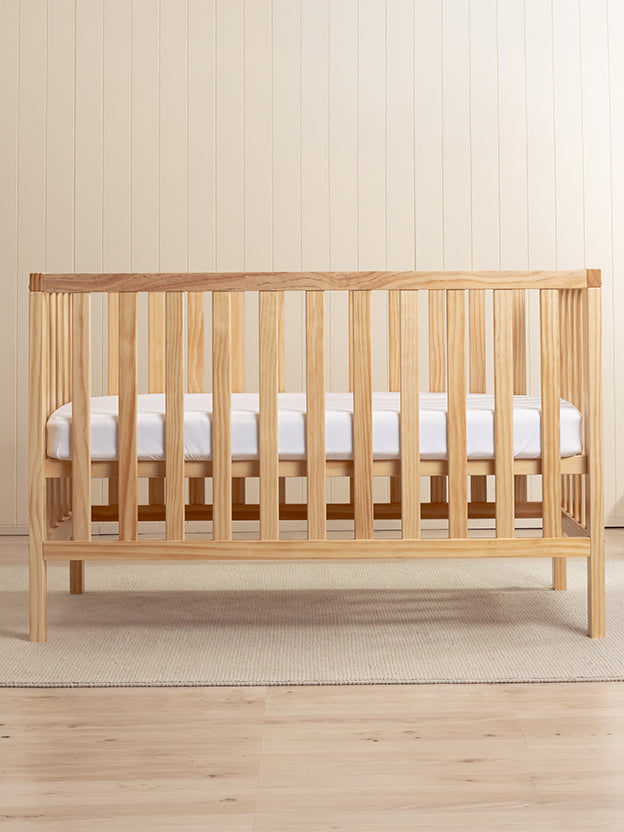Wooden cot with white mattress in a neutral room
