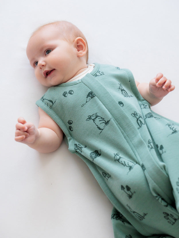 Baby smiling wearing a green 100% merino sleeping bag with bunnies on it
