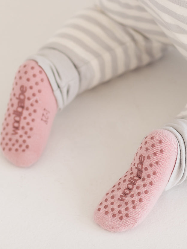 two feet wearing pink grippy socks with woolbabe logo