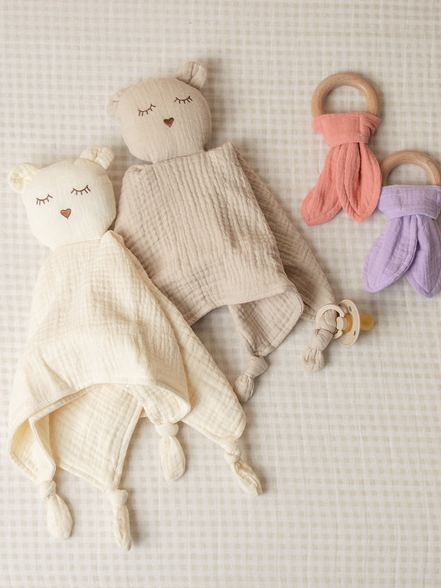 Two muslin sleepy bear comforters with two teething rings on a gingham background
