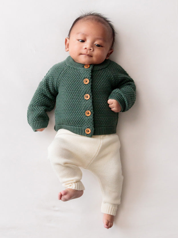 Baby wearing forest green merino knit cardigan and white merino knit pants