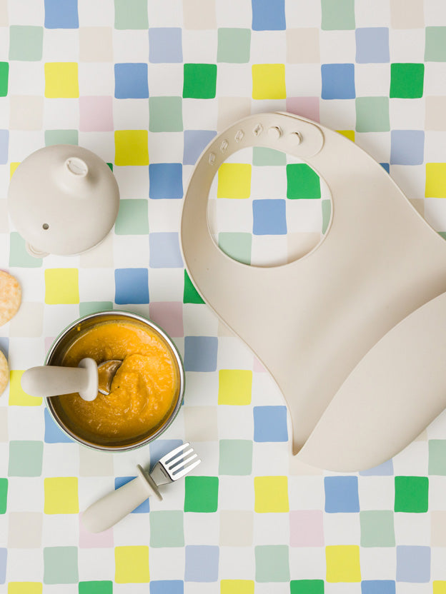 Starting solids essentials - a silicone bib, stainless steel bowl and cutlery on a checkered cloth