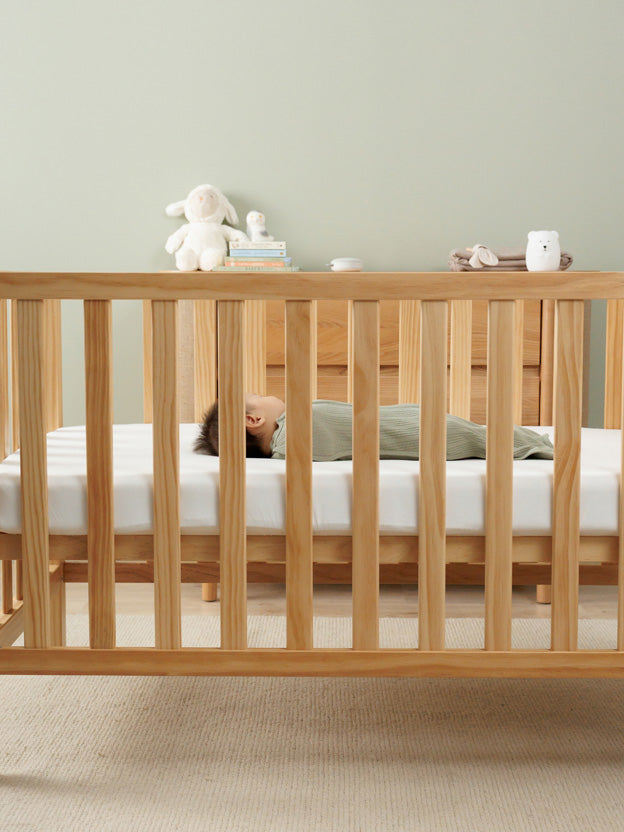 Baby asleep in wooden cot in a nursery setting