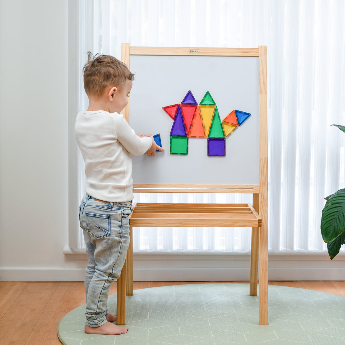 Child playing with colorful Connetix magnetic shapes on a wooden easel.