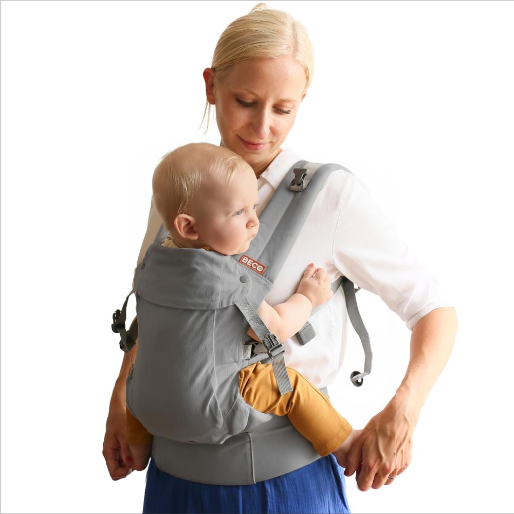 Woman carrying a baby in a grey Beco baby carrier against a white background