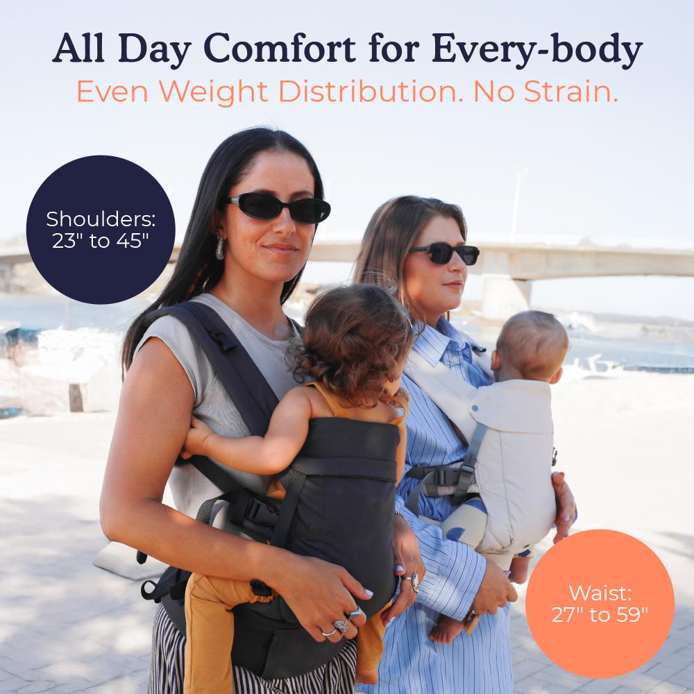 Two women with children using baby carriers by a waterfront.
