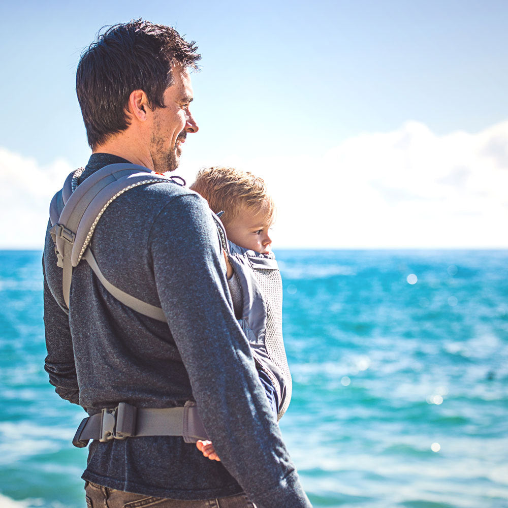 Man carrying a child in a mesh toddler carrier by the ocean