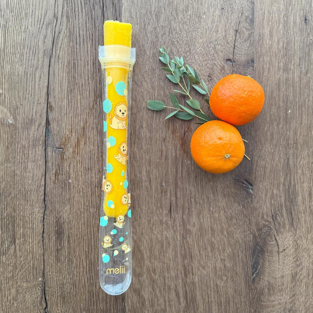 Yellow and clear melon baller with cartoon designs on a wooden surface with two oranges and a sprig of mint.