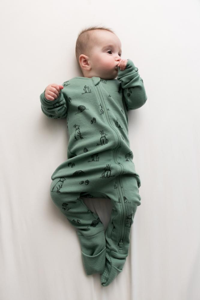 Baby wearing a green onesie with animal patterns on a white background