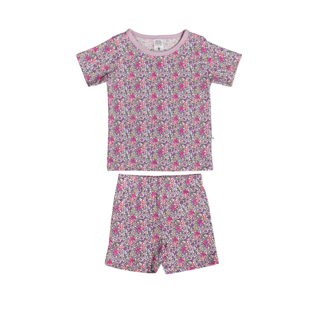 A two-piece baby pajama set featuring a short-sleeve t-shirt and matching shorts in a dense pink, purple, and white floral print on a light grayish-purple background.