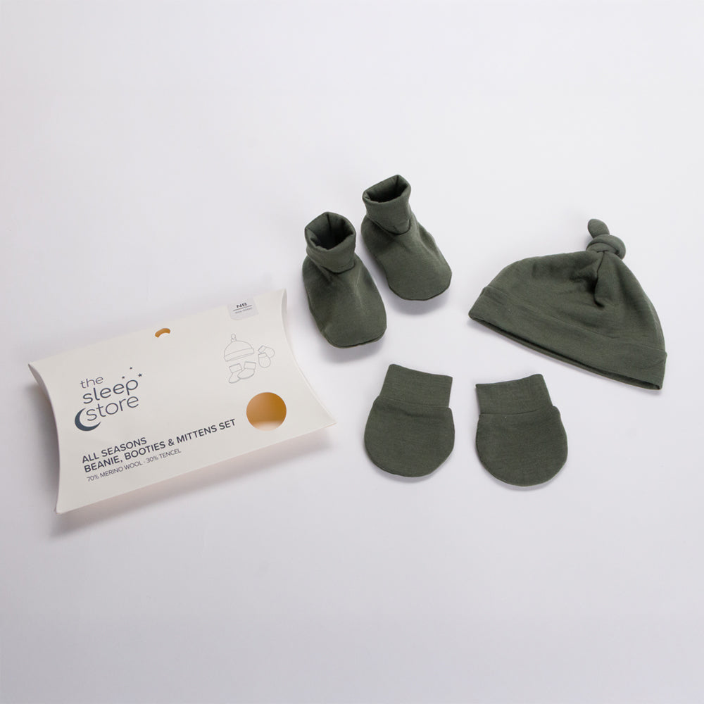 An olive green baby merino set including booties, a beanie, mittens, and a branded white packaging box on a clean white background.