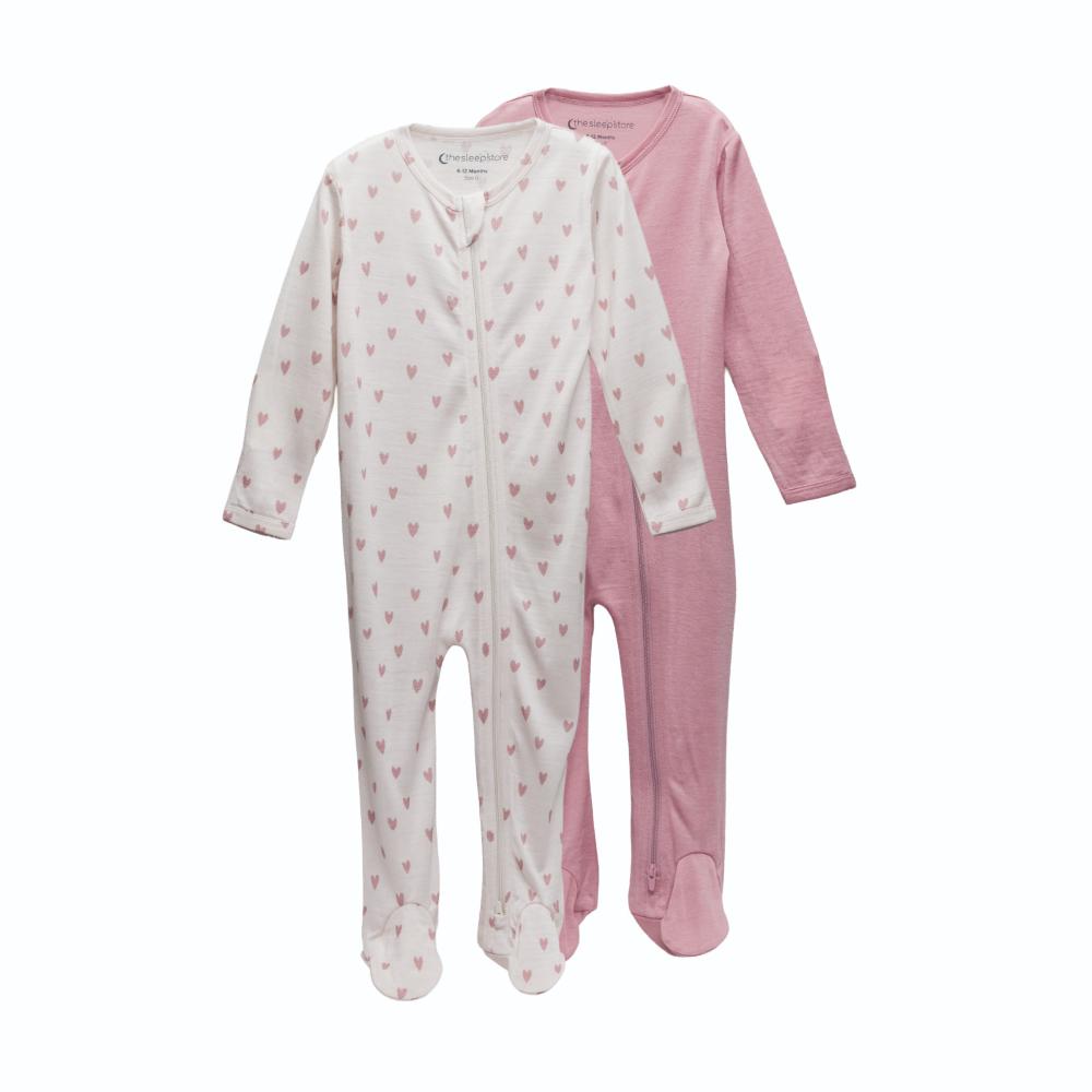 2 footed merino zipsuits, one pink, one cream with pink hearts on a white background